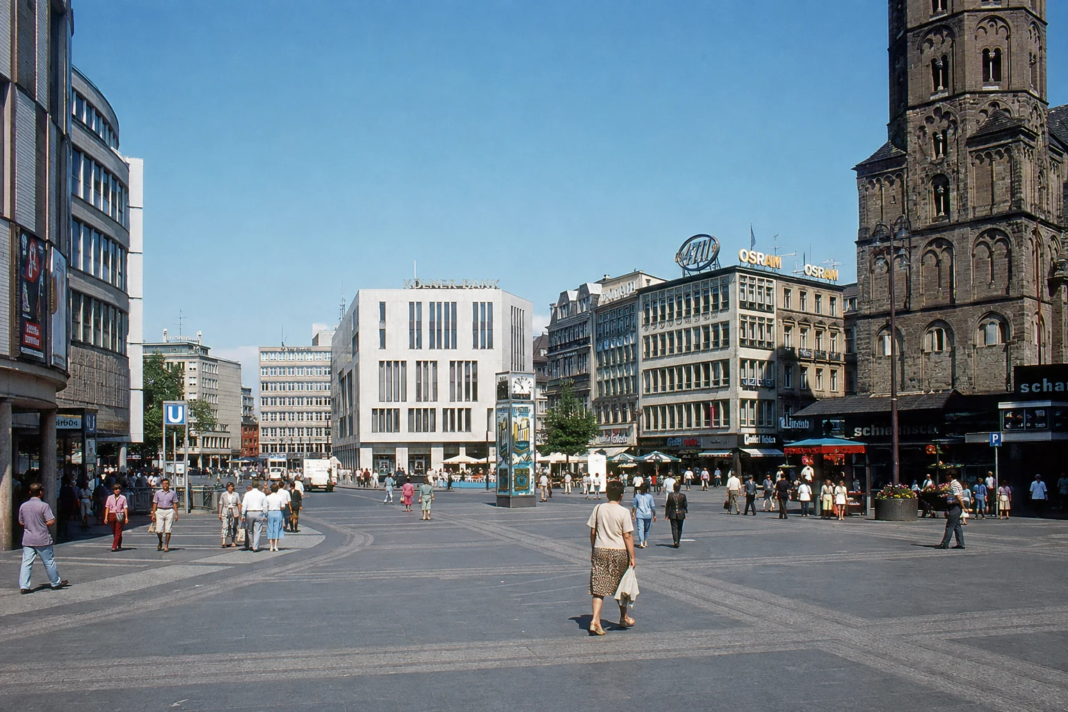Weiträumiger Kölner Innenstadtplatz mit Nachkriegsarchitektur, Passanten und romanischem Kirchturm