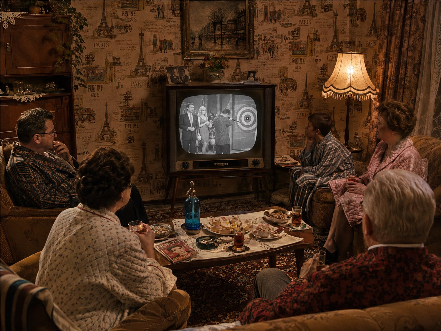 Familie in einem dicht gemusterten Wohnzimmer der fünfziger oder frühen sechziger Jahre vor einem kleinen Schwarzweißfernseher