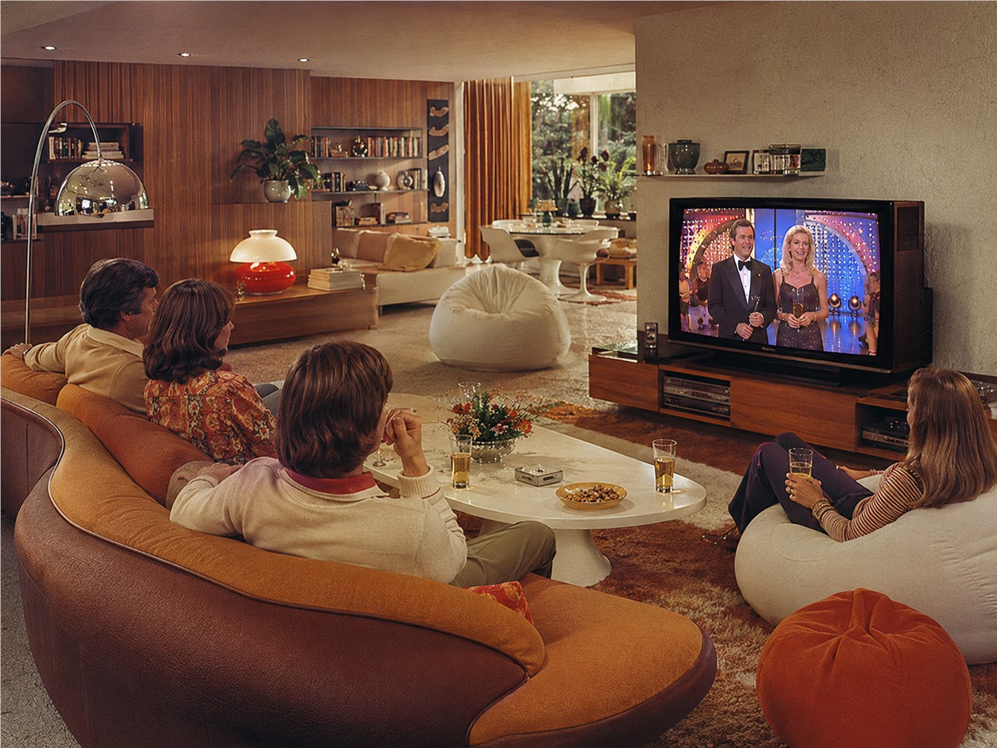 Familie vor einem Fernseher in einem Wohnzimmer der siebziger Jahre